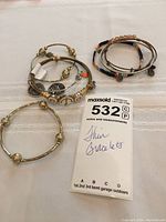 Overall view of seven thin bracelets of various styles laid on a white fabric surface, with the MaxSold tag indicating the lot number and description.