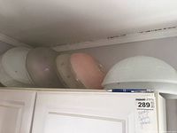 Five vintage ceiling globe light covers stacked on top of a cabinet, showing variety of pink, clear, and white colors and dome shapes.