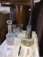 Set of three glass decanters and three ice cream glasses on a table with a cream patterned tablecloth, showcasing the shape and condition of each item.
