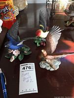 Photo showing three detailed Lenox bird figurines, including a brown eagle, a colorful bird with red and yellow coloring, and a blue bird on leafy bases, with MaxSold tag indicating Pretty Birds #2