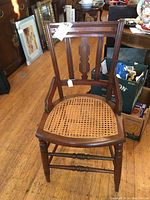 Full front view of the wooden chair showing caned seat and decorative carved backrest.