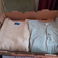 Two folded sweaters/t-shirts placed in a cardboard box, showing light brown Jack & Jones and gray J.Crew garments