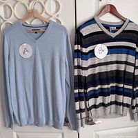 Two men's sweaters hanging on wooden hangers on a door, labeled A and B for identification, showing front view.