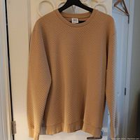 Beige textured sweater from ZARA hanging on black hanger against white wall