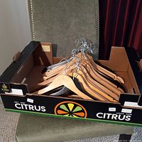 Box holding 20 wooden clothes hangers with silver metal hooks, arranged together.