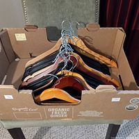 Box filled with 20 wooden clothes hangers in multiple wood finishes and colors, showing metal hooks and smooth surfaces.