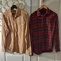 Both shirts hanging side by side; camel coloured RW & CO shirt and red and black checkered flannel J.CREW shirt.