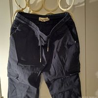 Front view of the dark blue men's pants hanging on hooks showing drawstring waist and pockets.