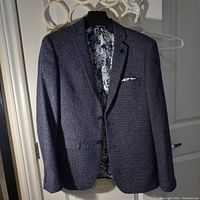 Photo of the front of dark blue speckled dressy jacket by Strauss on hanger, showing button front and chest pocket.
