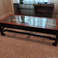 Front and side perspective of rectangular glass coffee table with wooden frame and legs, viewed on carpeted floor.