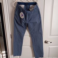 Men's blue cotton pants by J.Crew size 33x32, hanging on a hanger against a white door. Pants appear to be in excellent condition, showing no signs of wear or damage.