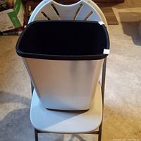 Front and top view of a large plastic garbage container placed on a white folding chair.