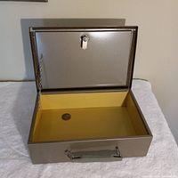 Open safe showing yellow interior lining, attached lid chain, and one coin inside.