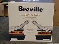 Front view of the Breville The Panini Duo box showing product name and image of the panini press with sandwiches inside.