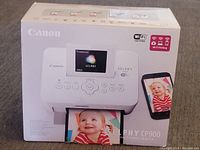 Canon Selphy CP900 printer box front showing printer and Wi-Fi print feature with sample photo output