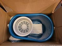Full view of open box showing blue bucket with white spinning wringer basket insert and mop components below.