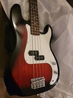 Close-up of the Huntington bass guitar body showing sunburst finish and white pickguard, four strings, and hardware.