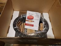 Boxed Karrsen Dome Oven in plastic wrap including instruction manual seen from top in open cardboard box.