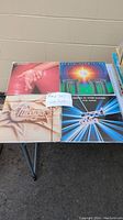 Four vinyl records: red cover with two clasped hands, Powerlight by Earth, Wind & Fire, Chicago VII by Chicago, As One by Kool & The Gang