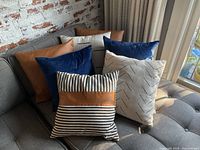 Seven accent pillows in a variety of colors and patterns arranged on a grey sofa showing front view.