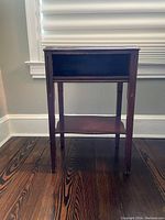 Front view of antique side table showing drawer, middle and lower shelves, and worn dark wood finish.
