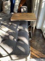 Side table positioned over dark gray tufted couch showing the zebra wood grain tabletop and metal frame.