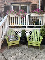 Two lime green Adirondack chairs positioned outdoors in front of a deck with railing and flower boxes.
