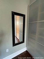 Vanity mirror mounted on a wall in a corner next to a closet or cabinet door, showing the frame detail and reflection.