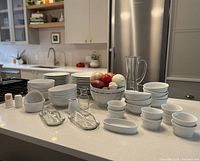 Overall view of all white dinnerware and serveware arranged on kitchen island