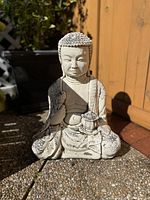 Front view of the cement Buddha statue showing detailed face and robe design in sunlight.