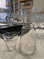 Clear glass water pitcher without handle on kitchen counter next to small insert glass, showing size and style.