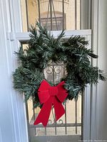 Single green artificial Christmas wreath with attached red bow hanging on a door/window, showing texture and style.