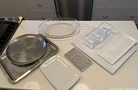Full view of all serving platters and trays arranged on a countertop including metal trays, ceramic and glass platters, and a glass condiment holder.
