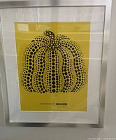 Close-up photo of the framed Kusama dotted pumpkin poster, showing the yellow background, black dotted pumpkin design, and artist/exhibit text.