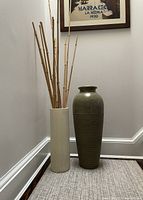 Two large vases, one green and ribbed, the other off-white cylindrical holding bamboo sticks in corner.