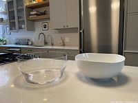 Wide shot of two large salad/serving bowls on kitchen countertop, showing glass and ceramic bowls side by side.
