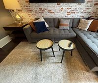 Wide photo showing two tripod coffee tables with woven cane-patterned tops placed on rug in front of sectional sofa.