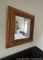 Square wall mirror with detailed antique wooden frame visible hanging on wall with reflection of room.