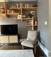 Full view of the Room & Board accent chair positioned near shelving and media console, showing the chair's profile and upholstery pattern.