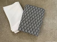 Two folded tablecloths, one plain white polyester, and one black and white patterned cotton.