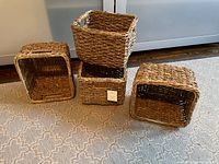 Four Threshold woven seagrass storage baskets stacked and spread on carpeted floor showing their shape and size.