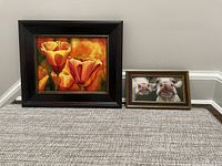 Two framed art prints against wall and carpet: tulips with black frame and cows with neutral brown frame.
