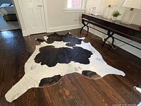full view of the cowhide rug laid out on dark hardwood floor showing black and white patterns and natural shape