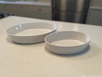 Two white oval serving bowls displayed side by side on a countertop, one larger and one smaller.