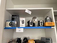 White shelving unit holding various cameras, lenses and flash units; upper shelf shows vintage box cameras and flashholder, lower shelf shows modern lens and flash boxes