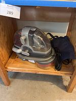 Bissell Spotbot portable carpet cleaner unit displayed on wooden shelf, showing overall condition and included hose and bag.