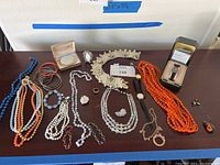 Overview of entire assortment of costume jewelry on table including necklaces, bracelets, rings, earrings, and watch.