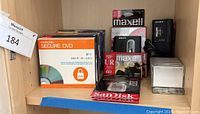 Photo showing packs of blank DVDs including Memorex Secure DVD 5-pack, Maxell blank DVDs, Sony mini cassette recorder, Sony cassette tape deck, Maxell UR 60-minute blank cassette tapes, blank mini cassettes in metal case, and SanDisk Extreme Pro memory card.