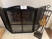 Three-panel black metal fireplace screen with mesh panels and two opening doors in the center. Fireplace interior and tile floor visible.