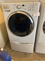 Front view of the Kenmore HE2t washing machine with storage riser drawer below shows control panel and machine door curving out from the body.